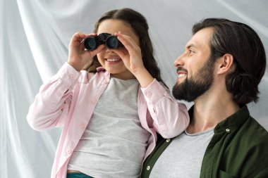 happy father looking at cute little daughter playing with binoculars clipart