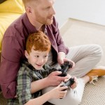 Blick aus der Vogelperspektive auf glückliche Vater und Sohn, die zu Hause am Steuerknüppel spielen Blick aus der Vogelperspektive auf glückliche Vater und Sohn, die zu Hause am Steuerknüppel spielen