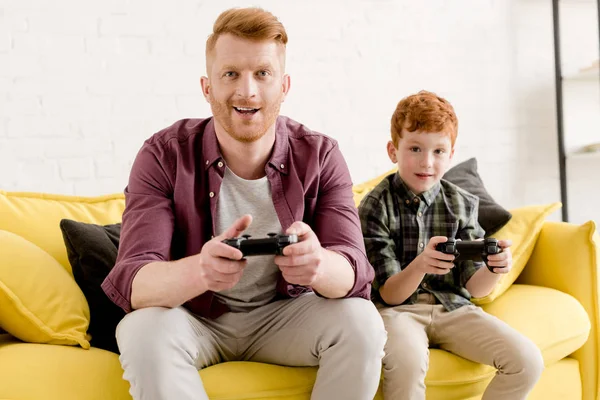 Feliz Padre Hijo Sentado Sofá Jugando Con Joysticks Casa —  Fotos de Stock