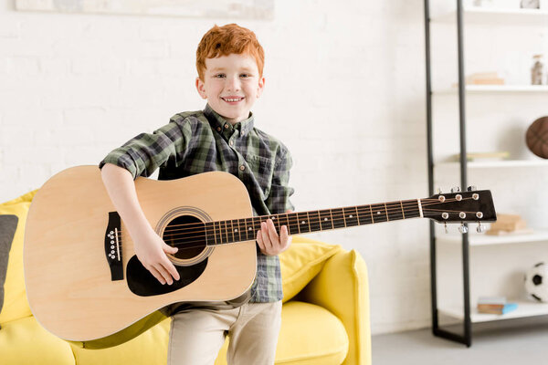милый мальчик держит акустическую гитару и улыбается в камеру

