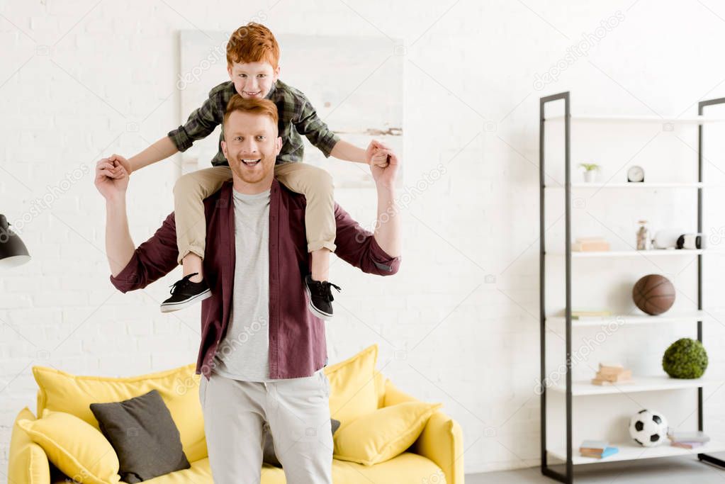 happy father carrying adorable smiling little son on neck at home