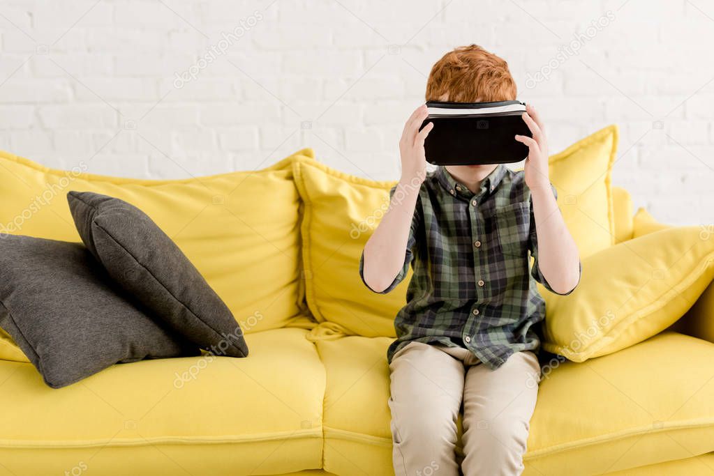 cute little boy in virtual reality headset sitting on couch