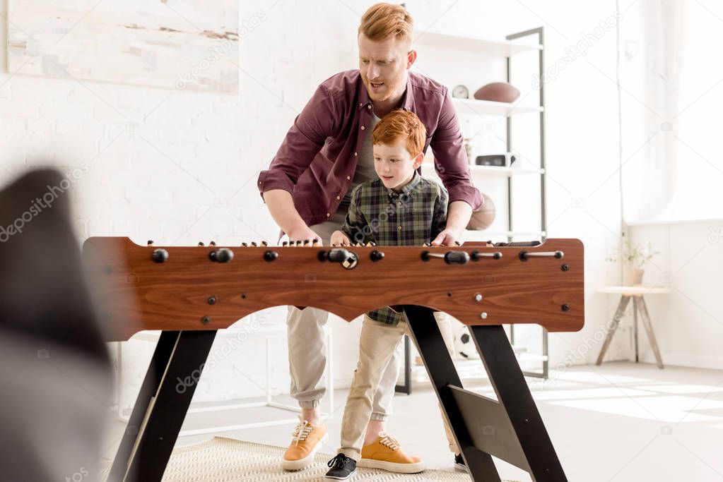 happy redhead father and son playing table football together at home