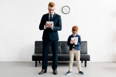 father and little son businessmen using digital tablets together clipart