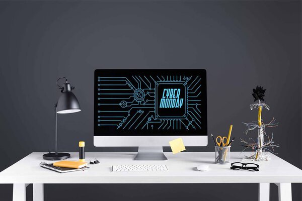 настольный компьютер с киберпонедельничной надписью на экране, лампой и офисными принадлежностями на столе на сером
