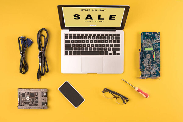 top view of laptop with inscription cyber monday sale only one day, smartphone, eyeglasses and wires on yellow