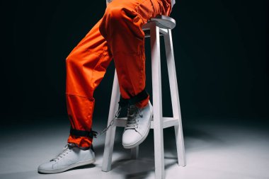 Adam turuncu görünümünü koyu arka plan taburede oturan bacaklar kelepçe ile Tekdüzen kırpılmış