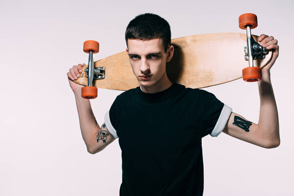 Hipster young guy holding longboard on shoulders isolated on white