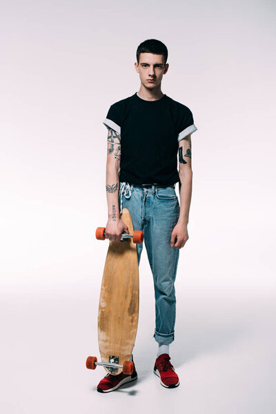Guy with tattooed arms holding longboard on white background