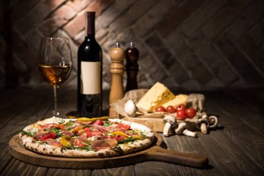 İtalyan pizza, baharat, peynir, domates ve şişe şarap ahşap yüzey üzerinde seçici odak
