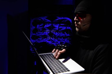 side view of hacker in eyeglasses using laptop with cables on background clipart
