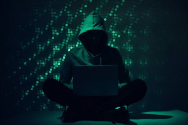 toned picture of silhouette of hacker in hoodie using laptop clipart