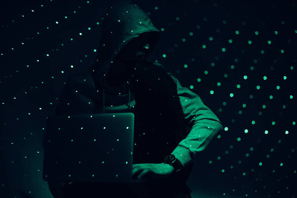 toned picture of silhouette of hacker in hoodie with laptop