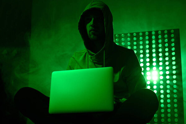 toned picture of male hacker in hoodie with laptop