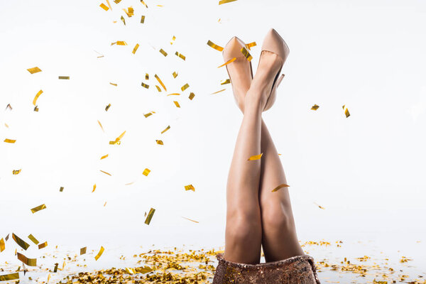 cropped image of woman lying with legs up under falling confetti on white