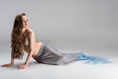 attractive woman with mermaid tail sitting on floor and looking away clipart