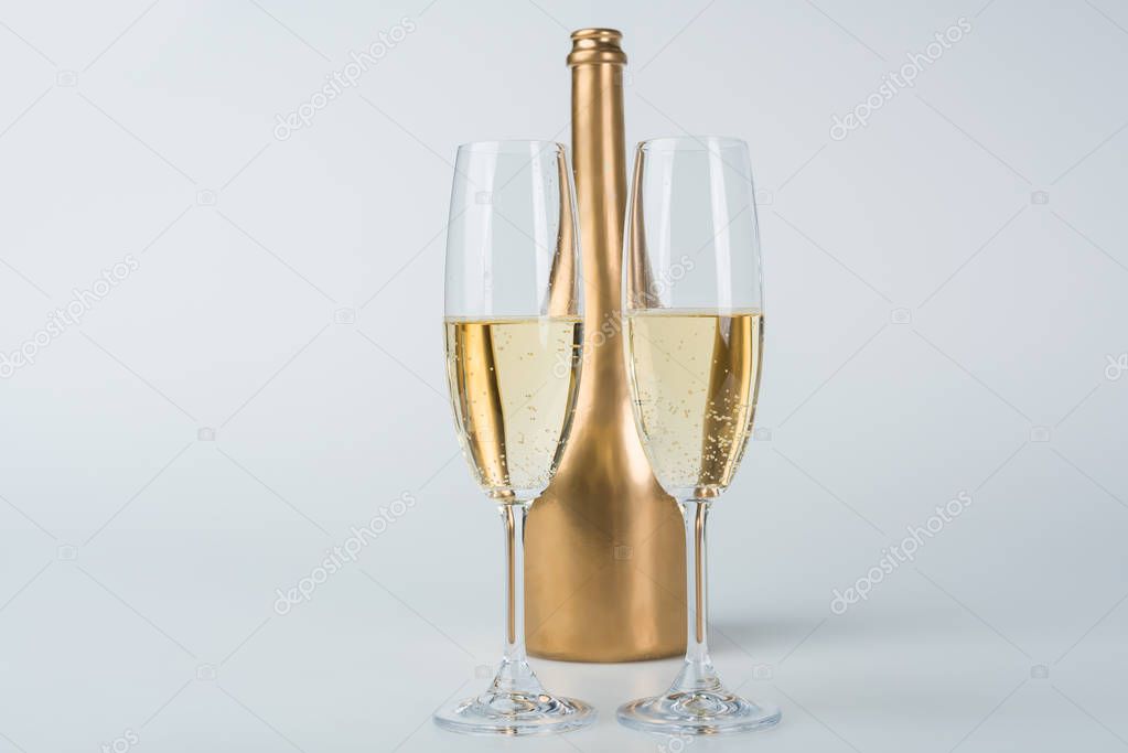 golden bottle of champagne and transparent glasses on white surface