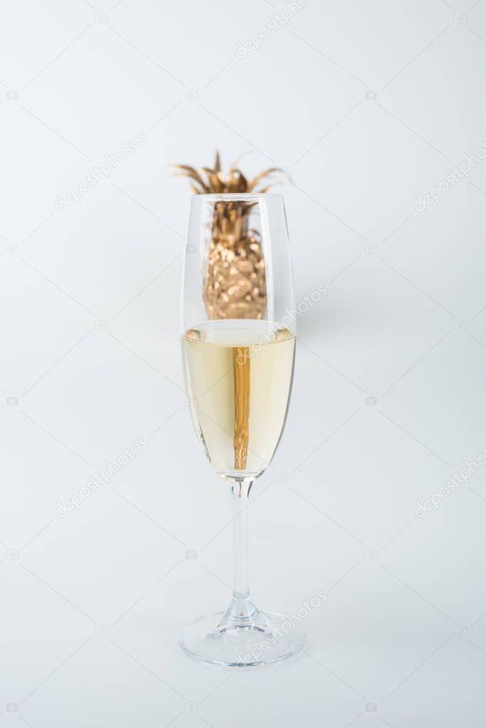 transparent glass of champagne and golden pineapple isolated on white