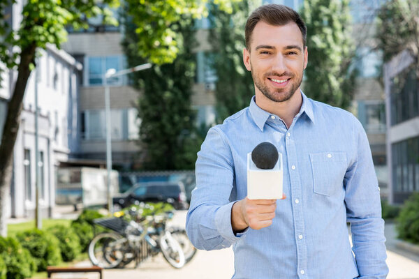 smiling male news reporter taking interview with microphone   