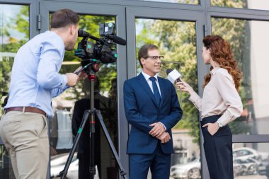 cameraman and news anchor interviewing businessman near office building  clipart
