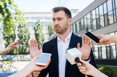 journalists interviewing serious businessman with microphones and smartphones  clipart