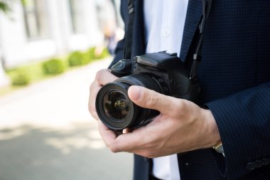 partial view of photojournalist in formal wear holding photo camera clipart