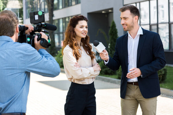professional cameraman and male news reporter interviewing smiling businesswoman  