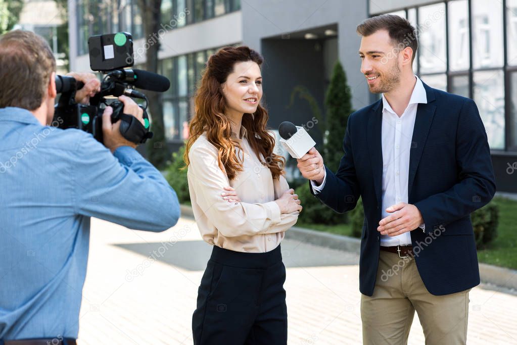 professional cameraman and male news reporter interviewing smiling businesswoman  