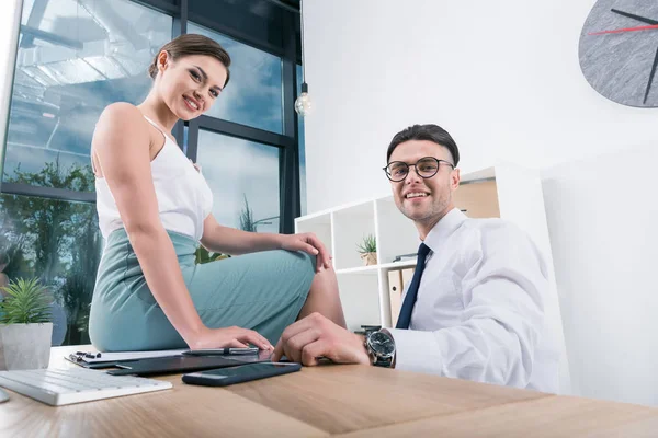 Empresarios sonrientes sentados en el lugar de trabajo en la oficina - foto de stock