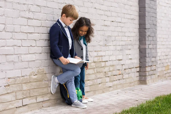 Multiethnic schoolkids reading book — Stock Photo