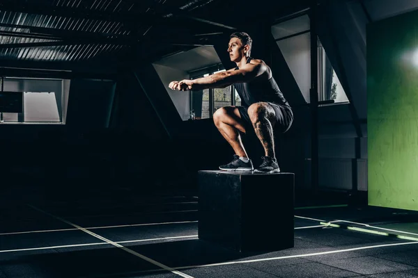 Sportsman doing squats on cube — Stock Photo