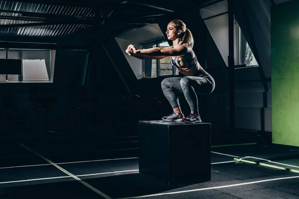 Sportswoman doing squats on cube — Stock Photo