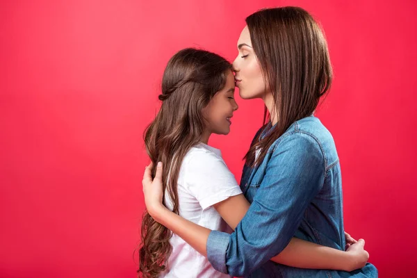 Madre besando hija en la frente - foto de stock