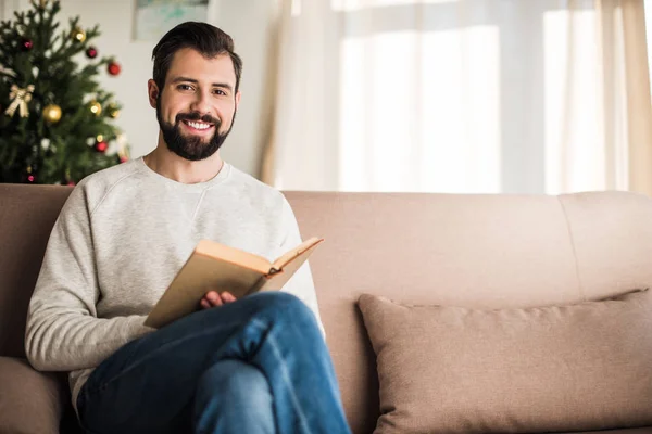 Handsome man reading a book at home and looking at camera — Stock Photo