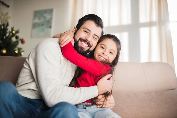 Feliz padre e hija abrazando y sentado en el sofá - foto de stock