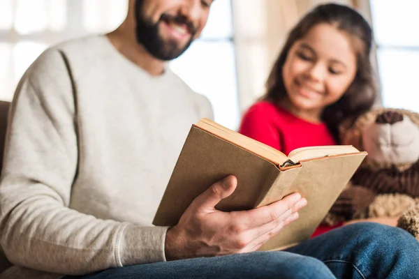 Обрезанный образ отца, читающего книгу дочери — стоковое фото