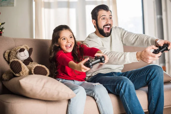 Padre e hija emocionados jugando videojuegos en casa - foto de stock