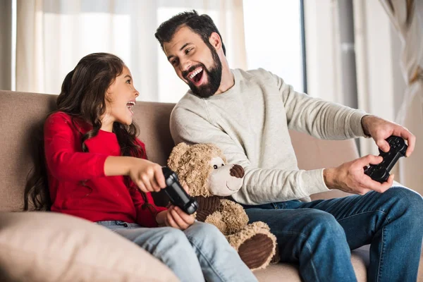 Pai feliz e filha jogando videogame em casa e olhando um para o outro — Fotografia de Stock