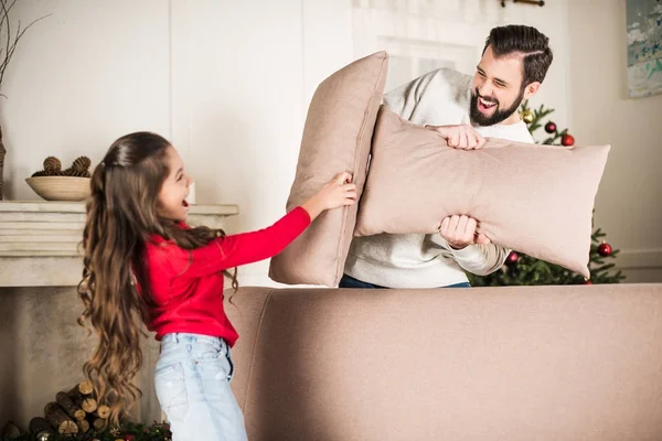 Father and daughter beating with sofa pillows at home — Stock Photo