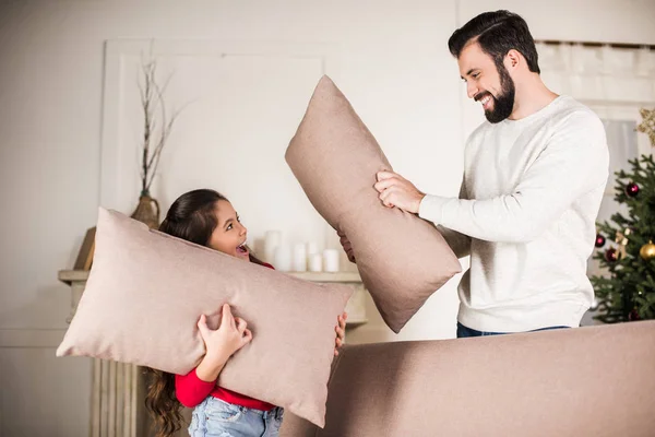 Padre e hija golpeando con almohadas en casa - foto de stock