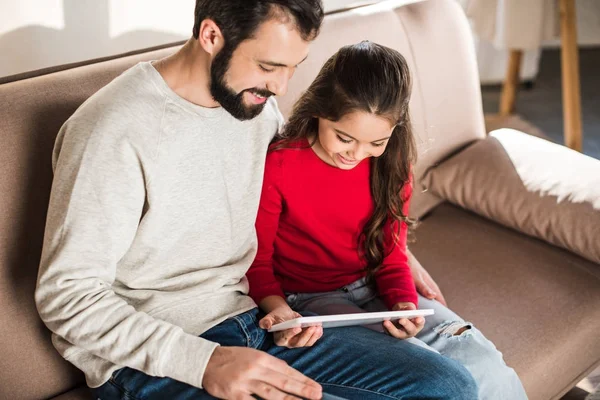 Father and daughter sitting on sofa and watching something on tablet — Stock Photo