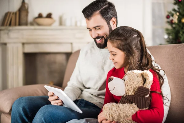 Father and daughter sitting on sofa and looking at tablet — Stock Photo