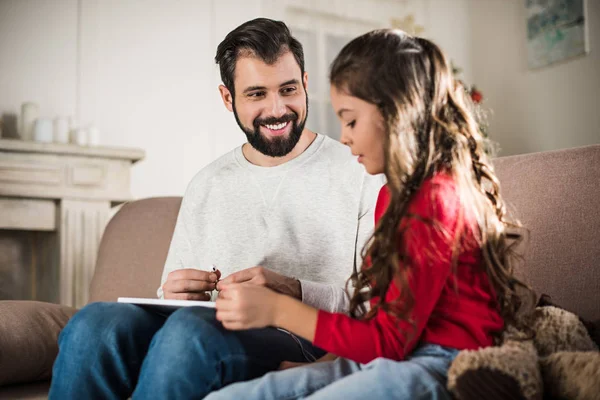 Tochter schaut auf Tablet und sitzt mit Vater auf Sofa — Stockfoto