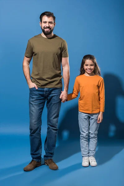 Padre e hija de pie y tomados de la mano en azul - foto de stock