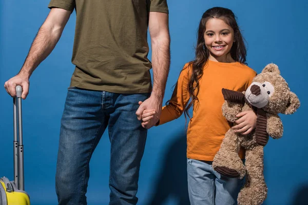 Cropped image of daughter and father standing and holding hands on blue — Stock Photo