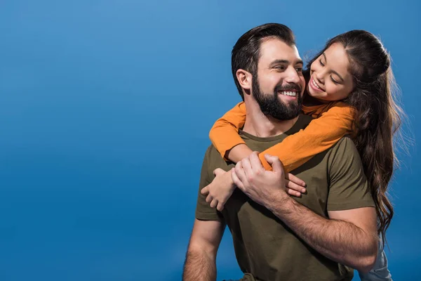 Schöner Vater gibt Huckepack an entzückende Tochter isoliert auf blau — Stockfoto