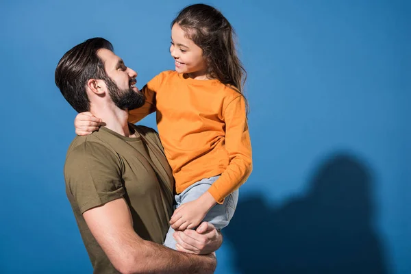 Handsome father holding smiling daughter on blue — Stock Photo