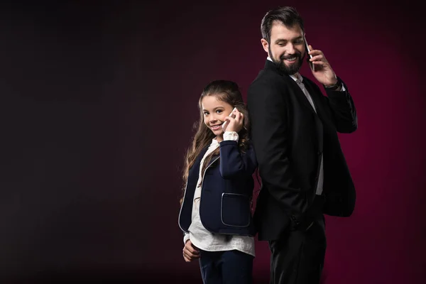 Father and daughter talking by smartphones on burgundy — Stock Photo
