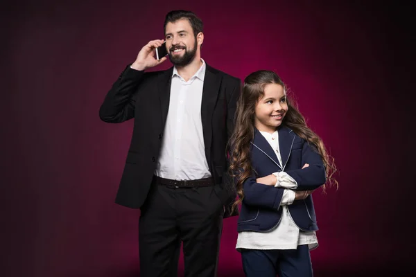 Vater spricht per Smartphone und Tochter steht mit verschränkten Händen auf weinrotem Grund — Stockfoto