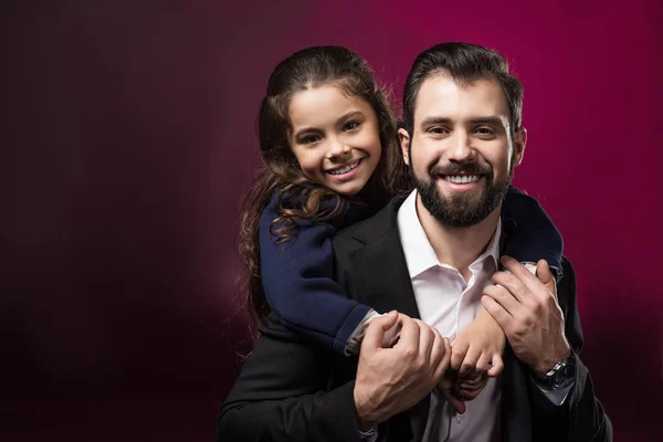 Daughter hugging father from back and they looking at camera on burgundy — Stock Photo